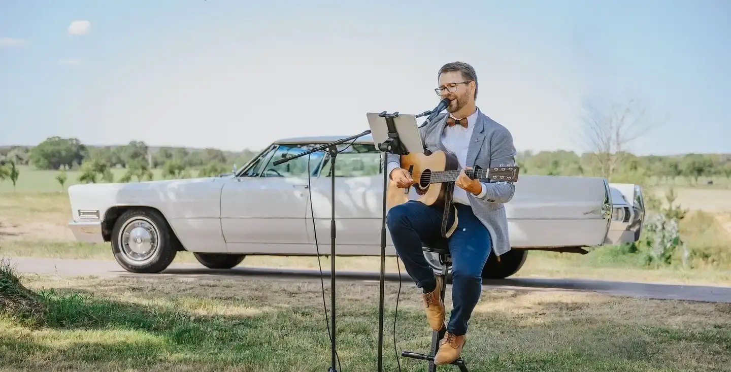 Sänger Mathias Gromeier spielt Live-Musik an der Gitarre vor einem Oldtimer-Hochzeitsauto